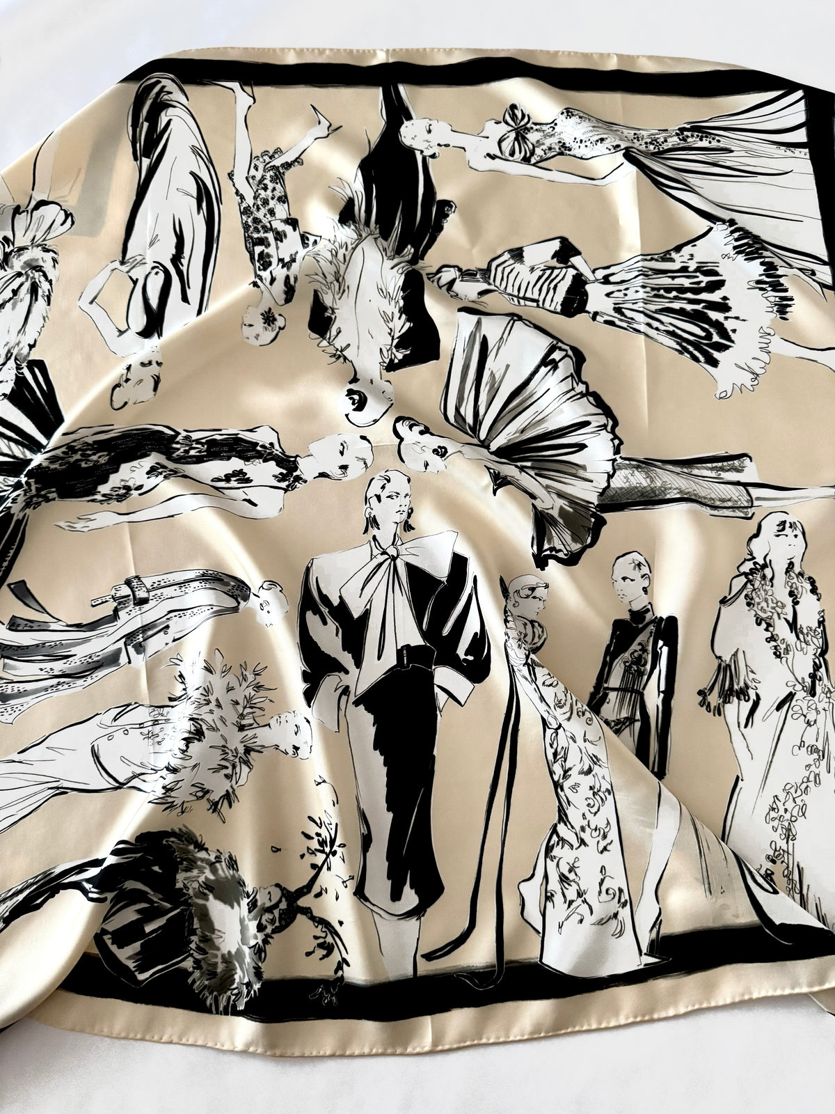 A square satin scarf with a beige background and a black-and-white fashion illustration print, laid flat on a white surface.